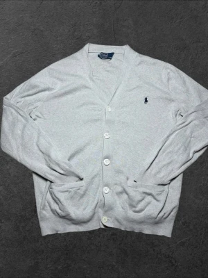 Polo Ralph Lauren finstickad kofta - herr strl M - Säljer en ljusgrå Polo Ralph Lauren finstickad kofta med knappar (show sample) i storlek M  👕 Märke: Polo Ralph Lauren 📏 Storlek: M 🎨 Färg: Ljusgrå 🧵 Material: 100% bomull 📐 Mått: Längd 67 cm, bredd 54 cm 📍 Skick: Bra skick. Lagad vid översta knappen, nedersta knappen utbytt samt liten obehandlad fläck på ryggen (se bilder)  💬 Har du några frågor är det bara att höra av dig! 💰 Vid snabb affär kan priset diskuteras. 📦 Skickar alltid inom 24 timmar!