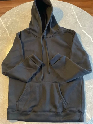 Svart hoodie - En stilren svart hoodie i 100 % polyester med mjuk och skön känsla. Medium-passform som sitter bekvämt och passar perfekt till vardag och fritid. Lättskött, hållbar och alltid rätt i stil.🔥