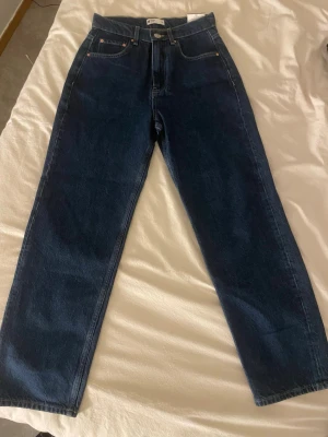 Mörkblå raka jeans från Weekday - Säljer ett par mörkblå jeans från Weekday med rak passform och hög midja. Klassisk femficksmodell med knappgylf och tydliga sömmar. Jeansen är gjorda i kraftig denim och har en stilren look som passar till det mesta.