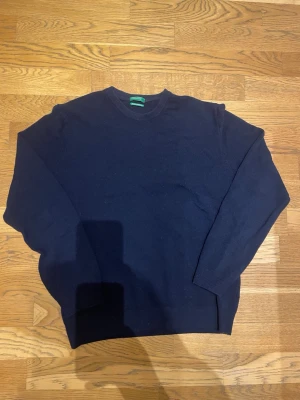 Mörkblå merinoulltröja  - Klassisk mörkblå stickad tröja från United Colors of Benetton i mjuk merinoull. Tröjan har rund halsringning och ribbade muddar vid ärmslut och nederkant. Perfekt för lager på lager och enkel att matcha med olika stilar.