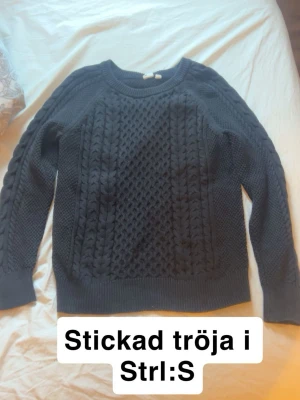 Mörkblå kabelstickad tröja S - Mysig svart kabelstickad tröja med rund halsringning och ribbade muddar. Tröjan har ett klassiskt flätmönster framtill och längs ärmarna, perfekt för lager på lager under kyliga dagar. 
