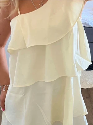 Volangklänning - Så fin klänning från Gina💛💛 bandet går att vika ner så de blir one shoulder klänning. Köpt förra året och är använd en gång och precis som ny! Storlek 164 men passar perfekt på mig som vanligtvis har XS🥰