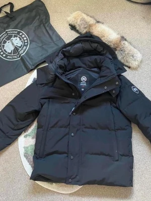 Svart dunjacka från Canada Goose - Snygg svart dunjacka från Canada Goose med avtagbar pälskant på huvan och klassisk logga på ärmen. Jackan har dragkedja och knappar framtill samt flera praktiska fickor. Perfekt för kalla dagar och riktigt varm.