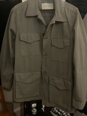 Grön overshirt A Day's March - Stilren grön overshirt från A Day's March med fyra stora fickor framtill och klassisk krage. Perfekt att bära öppen över en t-shirt eller stängd för en mer dressad stil. Storlek S. Pris kan diskuteras och ställ gärna frågor