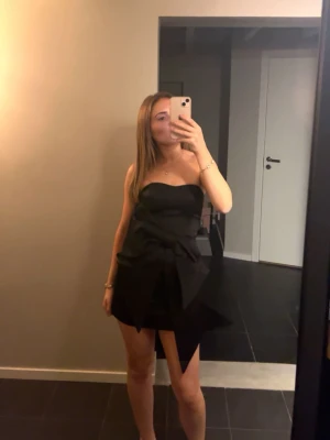 Svart axelbandslös klänning med rosett - Stilren svart axelbandslös kortklänning med en rosett framtill. Har tyvärr blivit för liten så måste sälja💕💕perfekt till middag eller fest 