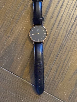 Svart klocka från Daniel Wellington - Stilren klocka från Daniel Wellington med svart urtavla och svart läderarmband. Boetten är i roséguld och har minimalistiska detaljer. Perfekt accessoar för dig som gillar klassisk och enkel design.