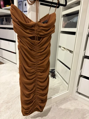 Brun draperad  från Zara - Säljer en snygg brun kortklänning från Zara med tunna axelband och drapering.. Klänningen har en rynkad effekt framtill och är figurnära med en cool, trendig look. Perfekt för dig som vill sticka ut med en unik stil.