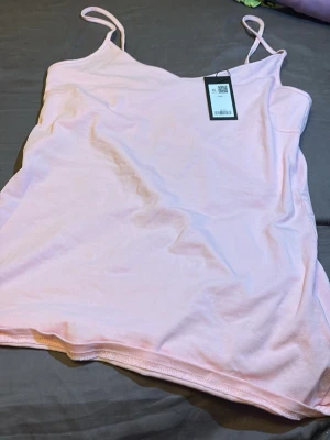 Ljusrosa linnetopp med smala band - Söt ljusrosa linnetopp med tunna axelband och enkel, rak passform. Perfekt för varma dagar och enkel att matcha med olika stilar. Mjuk och skön känsla i materialet.