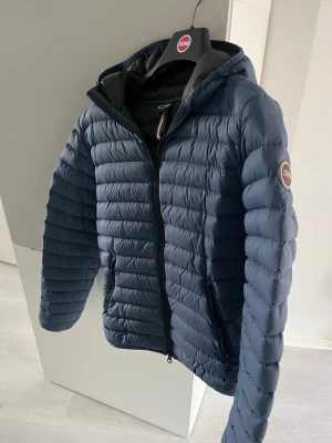Colmar dunjacka  - Snygg blå dunjacka från Colmar i otroligt bra skick med huva och dragkedja framtill. Jackan har quiltad design, två sidofickor med dragkedja och Colmar-logga på ärmen. Perfekt nu till våren men även till sommarkvällar och till hösten.          Nypris på cirka 3000kr