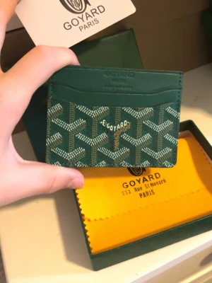 Grön plånbokl från Goy4ard - Snyggt grönt kortfodral från Goy4ard med det klassiska mönstret i vitt och beige. Tillverkat i exklusivt läder med flera kortfack och guldfärgad logga framtill. Perfekt för dig som vill ha en stilren och lyxig accessoar i fickan.