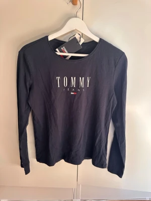 Mörkblå långärmad Tommy Jeans tröja - Fin långärmad topp från Tommy Jeans. Aldrig använt och prislappen finns fortfarande kvar. Storlek S