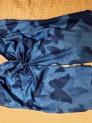 Blå topp med fjärilsmönster - Snygg blå topp med mörkare fjärilsmönster. Överdelen har knyt mellan kuporna för en trendig look. Materialet känns mjukt och följsamt mot huden.