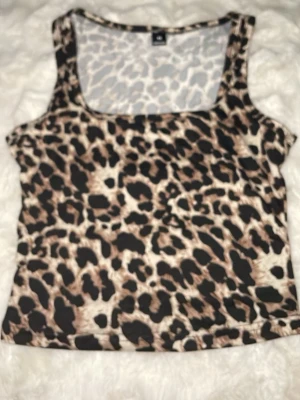 Leopardmönstrad linnetopp XS - Säljer en leopardmönstrad linnetopp i beige, brunt och svart. Toppen har breda axelband och rundad halsringning. Perfekt för dig som vill sticka ut med ett djurmönster i garderoben. Pris 20kr