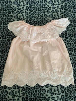 Ljusrosa off shoulder tröja  - Söt ljusrosa off shoulder tröja med bred volang och broderade spetsdetaljer både upptill och nedtill. Tröjan har en luftig passform och romantiska broderier som ger en feminin touch. Perfekt för sommarens varma dagar.