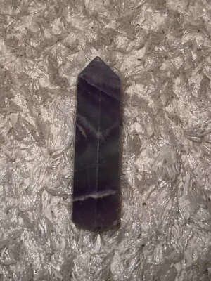 Lila spetsformad kristallstav - Säljer en lila kristallstav med spetsig topp och raka kanter. Kristallen har naturliga vita och mörklila band i stenen och är slipad till en avlång, sexkantig form. Perfekt som dekoration eller till kristallsamling.