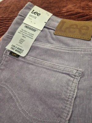 Helt nya! Vintage Lee Breese Flare high-waist corduroy lila byxor, storlek 31 31 - Säljer ett par ljuslila manchesterbyxor från Lee, modell Breese Flare. Byxorna har utsvängda ben, klassiska fickor och är tillverkade i mjuk manchester. Perfekta för dig som vill ha en retro och trendig look.