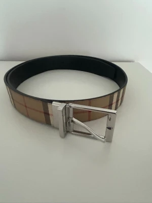 Beige rutigt bälte från Burberry - Nästan helt ny burrbery bälte, har haft den i nästan 2 månader och finns även kvitto. 105 cm och har absolut inga skador. För mer info/bilder så är det bara att höra av dig!