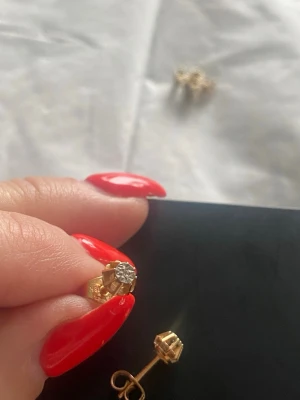 Diamantörhängen 18K flera guldstämplar/Guldörhängen med liten sten - HALLBETG’s GULD. Säljer ett par klassiska örhängen i guld med en liten äkta diamant i mitten. Örhängena har en enkel och tidlös design med stift och säkerhetslås. Perfekta för dig som gillar diskreta men eleganta smycken. Vintage.Förvarade i bankfack ej använda. (Investeringsobjekt)