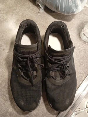 Svarta On Running sneakers - Snygga svarta sneakers från On Running med mesh-ovandel och unika CloudTec-sulor. Skorna har svarta snören och diskret logga på sidan. Perfekta för dig som gillar sportig och modern stil. Lätta och ventilerande material.