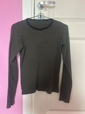 Randig långärmad tröja Brandy Melville - Säljer en svart och beige långärmad tröja från Brandy Melville. Tröjan har smala horisontella ränder och rund halsringning med svart kant. 
