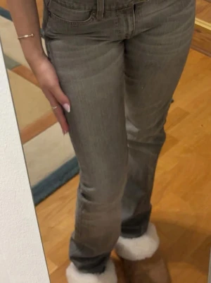 Grå bootcut jeans  - Säljer ett par grå bootcut jeans med snygg broderad detalj på bakfickan. Jeansen har klassisk femficksdesign och är tillverkade i denim med stretch för skön passform. Perfekta för dig som gillar en avslappnad och trendig look.