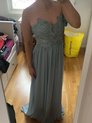 Blå balklänning  - Säljer en ljusblå långklänning med axelbandslös design och vacker spetsdetalj upptill. Klänningen har en flowy kjol och blommigt mönster på livet, perfekt för speciella tillfällen. Materialet känns lätt och faller snyggt. Finns så att man kan fästa axelband i klänningen på insidan men har endast ett axelband kvar tyvärr så man får sy/köpa egna isåfall☺️