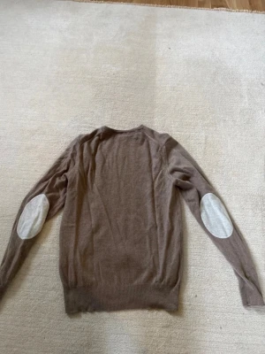 Stenströms merino tröja - Säljer en beige stickad merino tröja från Stenströms med rund hals och långa ärmar. Tröjan har ljusa armbågslappar i kontrastfärg och ribbade muddar vid ärmslut och nederkant. Perfekt för en avslappnad och stilren look.