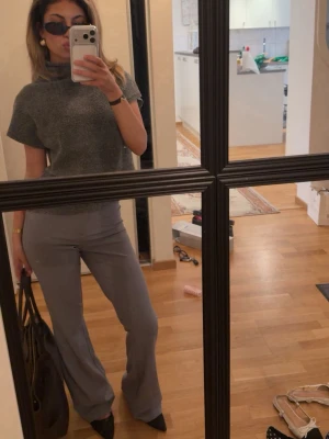 Grå stickad polotröja med kort ärm - Grå stickad polotröja med korta ärmar och hög krage. Tröjan har en avslappnad passform och är gjord i mjukt material som känns skönt mot huden. Enkel och stilren design som är lätt att matcha till olika outfits.