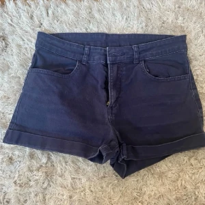Mörkblå denimshorts (jeansshorts)  - Snygga mörkblå denimshorts med uppvikta benslut och klassiska fem fickor. Shortsen har bälteshällor och stängs med knapp och dragkedja. Perfekta till sommaren och lätta att matcha med olika toppar.