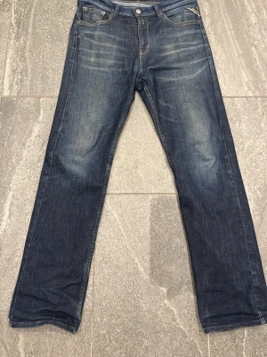 Avslappnade Replay jeans - Säljer ett par mörkblå jeans från replay med raka ben och klassisk femficksmodell. Jeansen har snygga slitningar framtill och kontrastsömmar på bakfickorna. Tillverkade i denim med en autentisk tvättad look. Perfekta för en avslappnad stil.