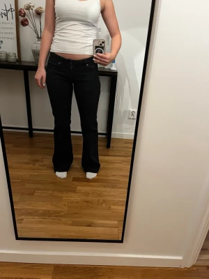 Svarta bootcut jeans med låg midja - Säljer ett par svarta bootcut jeans med låg midja. Jeansen har klassisk femficksdesign och sitter tight över låren för att sedan bli vidare nedtill. Perfekta för dig som gillar en retro och trendig look.