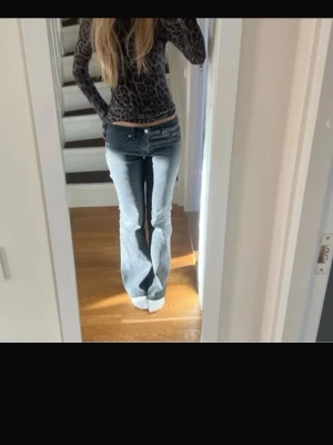 Blå bootcut jeans med låg midja - Säljer ett par svarta bootcut jeans med låg midja och klassisk femficksdesign. Jeansen har en snygg tvätt med ljusare partier framtill och utsvängda ben. Perfekta för dig som gillar retrovibbar och vill ha ett par jeans som sticker ut.