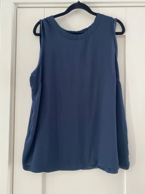 Mörkblå ärmlös topp - En enkel och stilren mörkblå linnetopp med rund halsringning och avslappnad passform. Toppen är ärmlös och har en mjuk, lätt struktur som passar perfekt till sommaren. Inga synliga detaljer eller mönster, bara clean vibes. Toppen är väl använd och färgen har blekts på bakstycket i övrigt i bra begagnat skick  Mått Över bröstet: c 58 cm Längd från axeln och ner: ca 69 cm  Lyocell, viskos och polyester  Kommer från ett djur och rökfritt hem