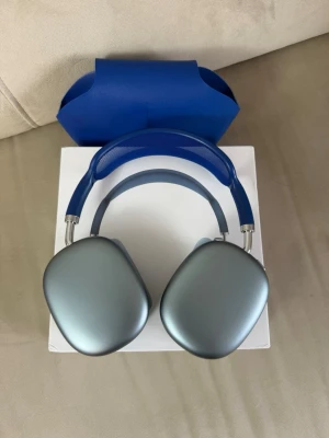 Apple AirPods Max blå hörlurar - Snygga Apple AirPods Max i blått med mjuka öronkuddar och justerbart huvudband i mesh. Hörlurarna har en stilren design i aluminium och rostfritt stål, samt medföljande blåt skyddsfodral. Perfekta för dig som vill ha grymt ljud och modern look.