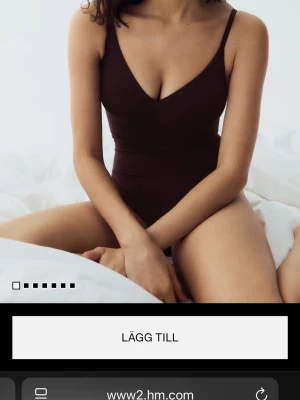 Mörkbrun body med smala axelband - Snygg mörkbrun bady från H&M med smala axelband och djup urringning fram. Klassisk, enkel design utan mönster och med en kroppsnära passform. Perfekt för dig som gillar stilrena badkläder. Materialet är troligtvis en stretchig syntetblandning som torkar snabbt.