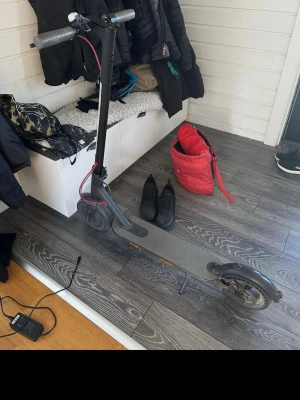 Svart elscooter med laddare - Säljer en svart elscooter med grå detaljer och röd bromskabel. Scootern har en robust ram i metall och medföljer laddare. Perfekt för att ta sig runt snabbt och smidigt i stan. Stilren design och enkel att använda.