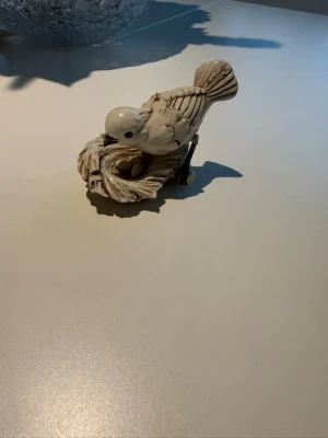 Keramikfågel på bo av Velardi - Dekorativ keramikfigur föreställande en vit fågel sittande på ett bo med ägg. Skulpturen har handmålade detaljer och är signerad Velardi undertill. Perfekt som prydnad i hemmet för dig som gillar naturinspirerad inredning.