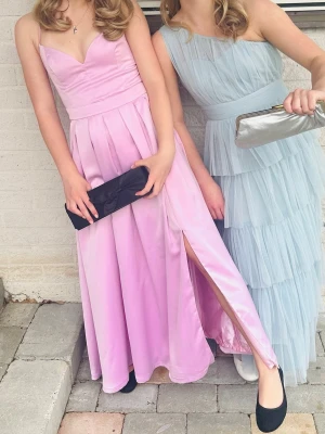 Ljusrosa långklänning med slits - Elegant ljusrosa långklänning med v-ringad överdel och smala axelband. Kjolen har fina veck och en hög slits på ena sidan som ger en snygg touch. Perfekt till bal eller student. Bara använd två gånger. Priset kan diskuteras vid en snabb affär.