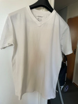 Vit v-ringad t-shirt från Livergy - Klassisk vit t-shirt från Livergy med v-ringning och korta ärmar. Tillverkad i mjuk bomull som känns skön mot huden. Enkel och stilren design som passar till det mesta. Perfekt basplagg för garderoben.