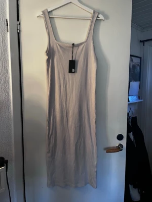 Ljusribbad långklänning med breda axelband - Säljer en ljus, ribbad långklänning med breda axelband och fyrkantig ringning. Klänningen har en enkel och stilren design som passar perfekt till sommaren. Materialet är mjukt och stretchigt för en bekväm passform.