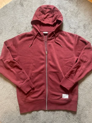 Solid vinröd hoodie med dragkedja  - Snygg vinröd hoodie från Solid med dragkedja framtill, två stora fickor och justerbar huva med snören. Tillverkad i mjukt bomullsmaterial som känns skönt mot huden. Perfekt för en avslappnad och stilren look. Storlek S men passar som M ungefär 