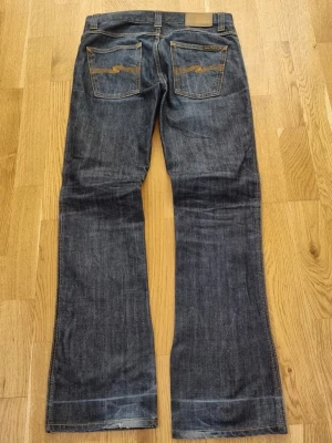 Nudie jeans Slim Jim bootcut - Säljer dessa nudie jeans i modell slim Jim. De sitter ganska rakt slim med bootcut. Dessa är dry broken och säljs inte längre hos nudie. Jeansen är väl använda av mig och har fått lite patina. Storlek enligt lapp: 30/32. Måtten i cm: Längd 100, midja 39, benöppning 21. De har två pyttesmå hål i grenen som lätt kan bli lagade på en av nudie jeans affärer. De var även uppsyddaförut och har därför ett streck nere vid fållen. Jag h att töjt ut de för att göra jeansen mer boot. Tveka inte vid frågor!