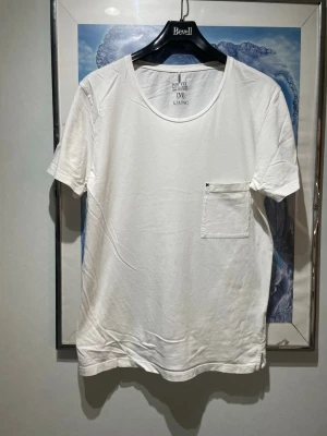 Vit t-shirt från Ljung med bröstficka - Klassisk vit t-shirt från Ljung med rund halsringning och en enkel bröstficka på vänster sida. Tillverkad i mjuk bomull och har en normal passform. Perfekt basplagg för alla tillfällen.har kostat 400kr 