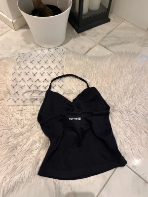 Svart linnetopp från DFYNE - Snygg svart linnetopp från DFYNE med smala axelband och diskret logga framtill. Toppen har en lätt v-ringad form och är tillverkad i ett stretchigt material som sitter bekvämt. Perfekt för en trendig och sportig look.