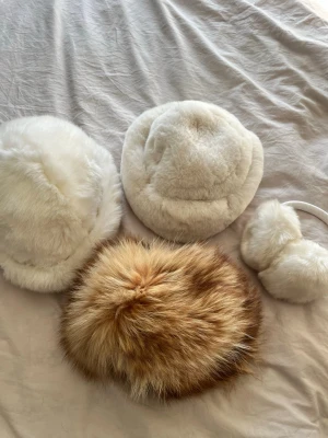 Fyra fluffiga pälsmössor och öronmuffar - Säljer ett set med tre fluffiga pälsmössor och ett par öronmuffar. Två mössor är vita en mössa är brunmelerad med längre päls och öronmuffarna är vit