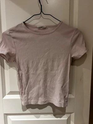 Ljusrosa basic t-shirt - En enkel ljusrosa t-shirt med rund hals och korta ärmar. Tillverkad i mjuk bomull som känns skön mot huden. Perfekt att matcha med jeans eller kjol för en avslappnad look.