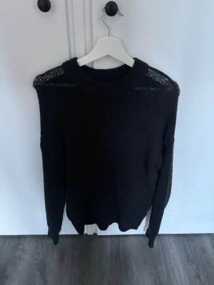 Svart stickad tröja från 157 - Den passar en som är M/L också. Snygg svart stickad tröja från 157 med rund halsringning och detaljer i meshstickning vid axlarna. Tröjan har lång ärm och en avslappnad passform, perfekt för lager på lager. Enkel att matcha till olika outfits.