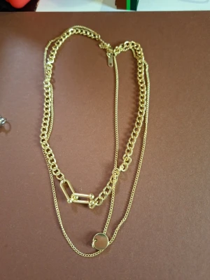 Guldigt lager-på-lager halsband - Snyggt guldigt halsband med två kedjor i olika tjocklekar. Ena kedjan har en rund platta som detalj och den andra har en unik länk med rektangulär form. Perfekt för dig som gillar trendiga accessoarer och vill ha något som sticker ut.