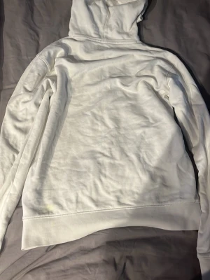 Vit hoodie med glasögon från C.P. Company - Säljer en vit hoodie från C.P. Company med dragkedja och ikoniska glasögon i huvan. Hoodien har två fickor framtill och logga på bröstet. Tillverkad i mjukt bomullsmaterial och har en clean, modern look som sticker ut. Den är 14 år men passar xs/s