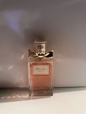 Miss Dior Eau de Parfum - Elegant parfym från Dior i en rektangulär glasflaska med ljusrosa doftvätska. Flaskan har en guldfärgad rosett vid halsen och ett genomskinligt lock. Klassisk och feminin design som utstrålar lyx. 30 ml. Ordinarie pris 839kr.